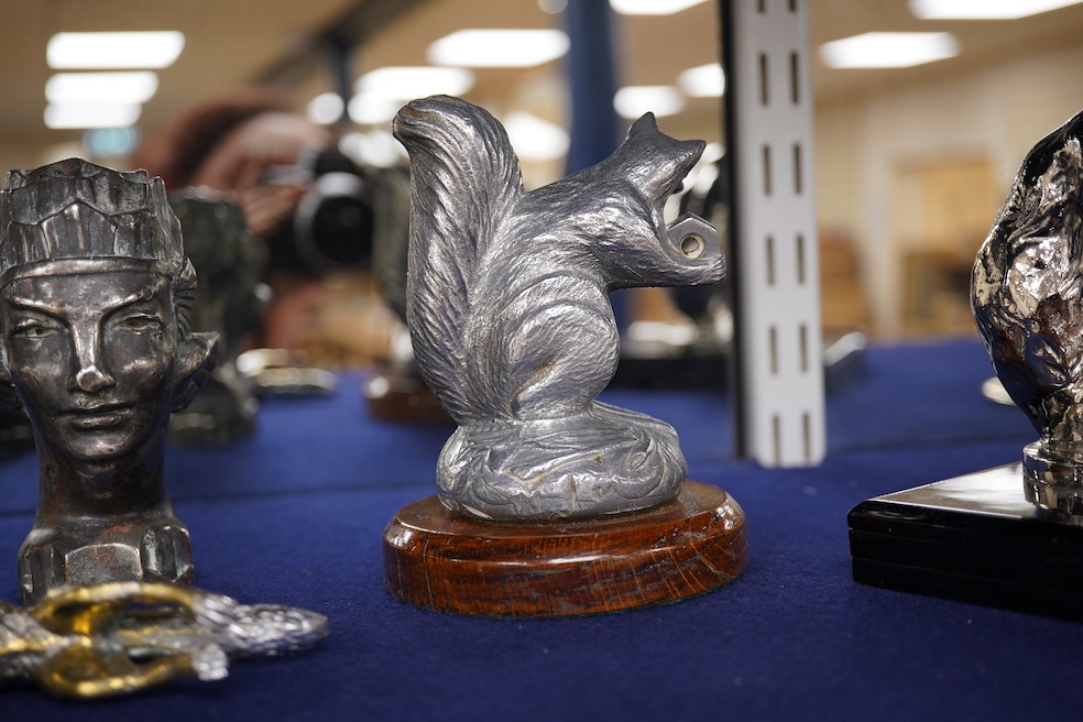 Seven chrome, brass and aluminium car mascots, etc. including an unusual and comical aluminium car mascot in the form of a squirrel holding a nut, together with a standing bear, an Art Deco winged head, a ram, a running